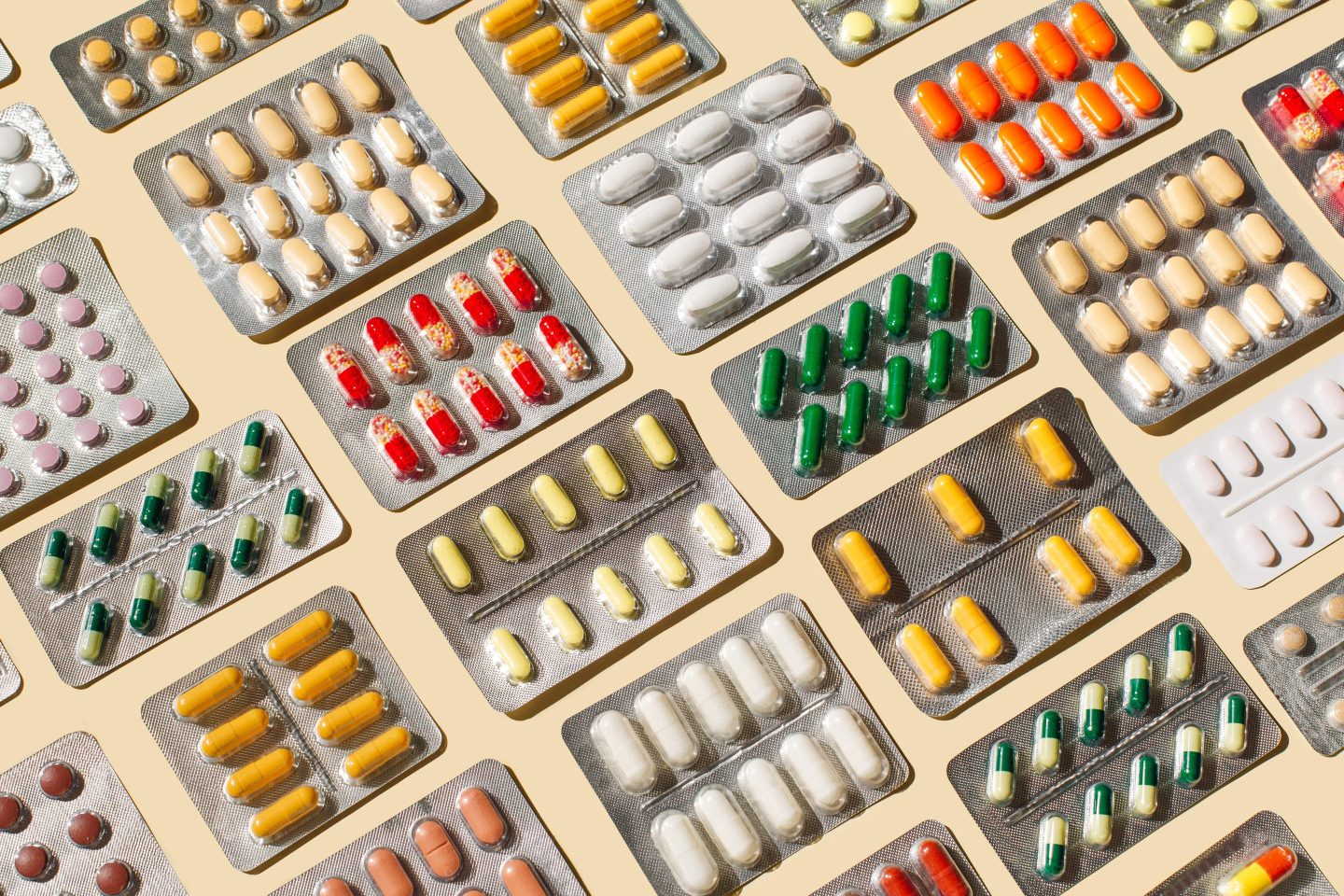 Pattern of colorful pills and capsules on beige background.