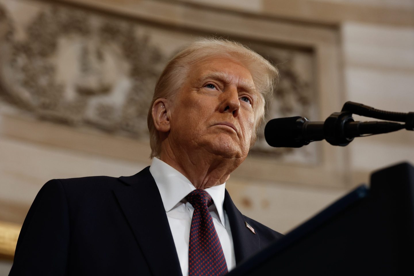 Closeup of Donald Trump in suit and tie, at a microphone