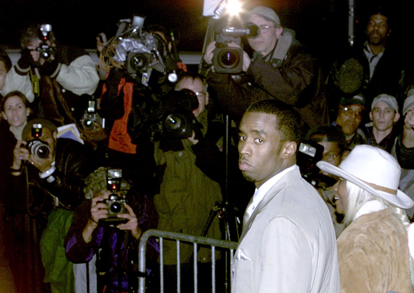 Sean Combs looks over his shoulder and standing behind him are numerous people taking photos of him.