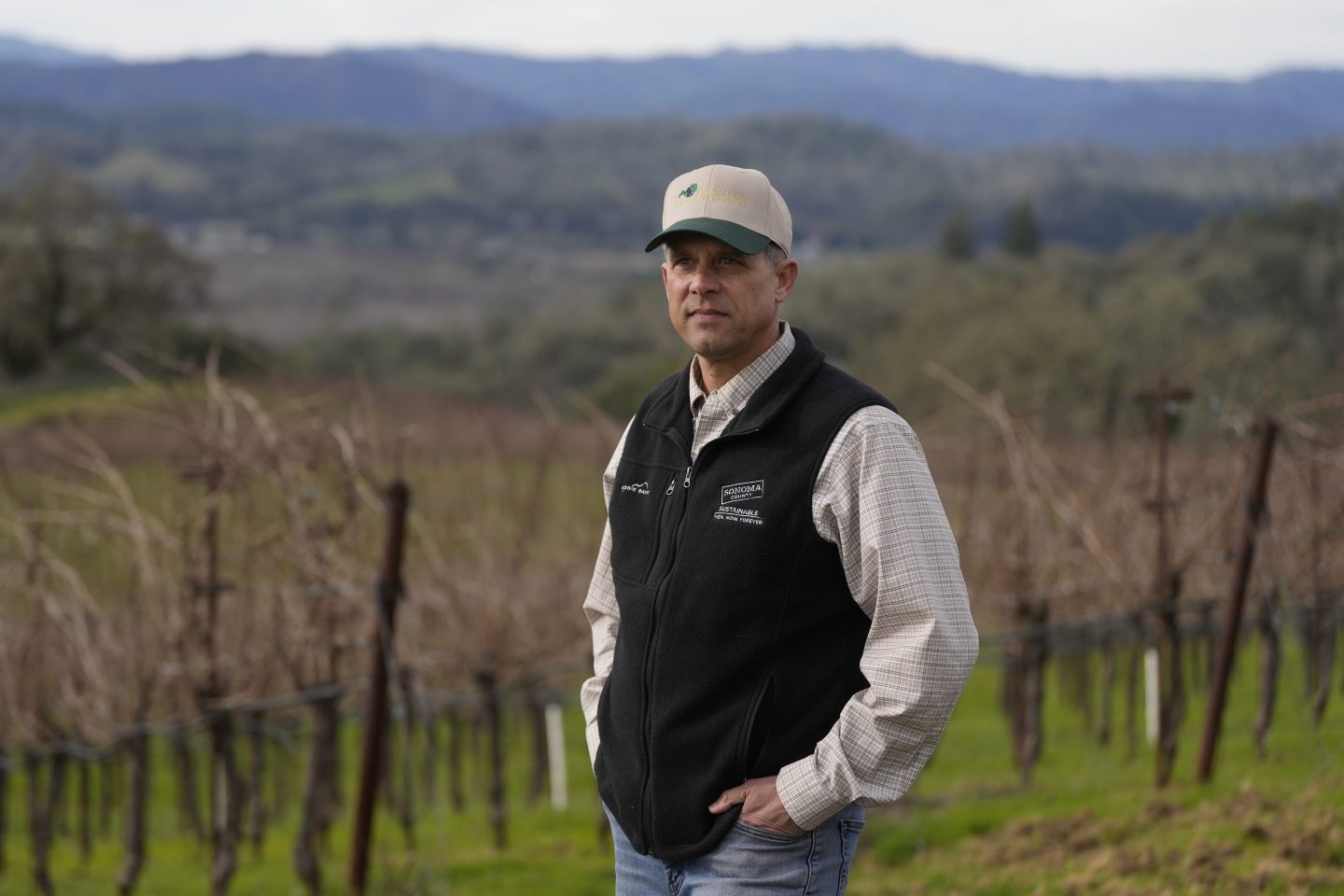 A winemaker stands in front of his farm and vineyard