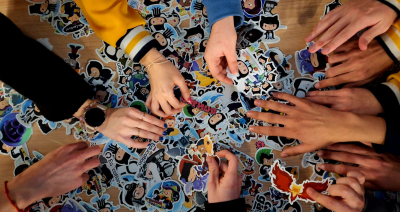 Several people's hands are reaching into a big pile of stickers on top of a table.