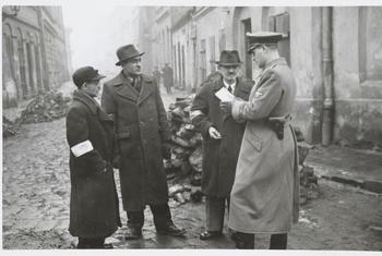 A German policeman checks the identification papers of Jewish people in the Krakow ghetto. Poland. Circa 1941.