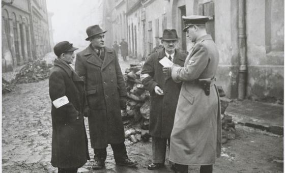 A German policeman checks the identification papers of Jewish people in the Krakow ghetto. Poland. Circa 1941.