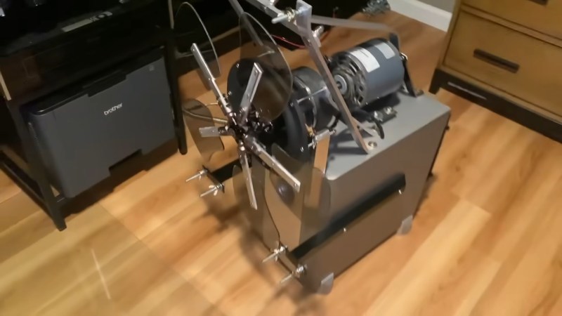 A rotary subwoofer made out of a speaker coil, a medium-size fan an a grey wooden box to stand on.