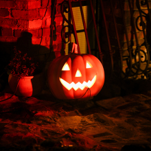 A glowing carved pumpkin sits against a brick wall in the dim light.