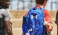 Three boys with their backs turned to the camera carrying Under Armour backpacks