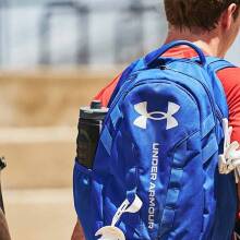 Three boys with their backs turned to the camera carrying Under Armour backpacks