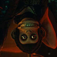 A creepy toy monkey stares out from behind a woman's spread legs. 