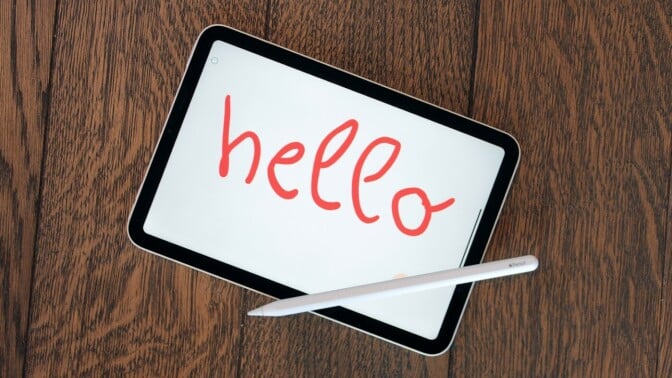 Apple iPad mini sitting on a table with the word "hello" written in red by a stylus pen.