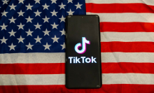 The TikTok app logo on a smartphone screen. The phone is laying on an American flag.