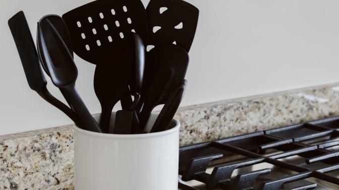 black kitchen utensils in a jar by a stove