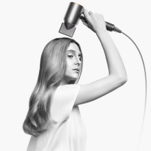 black and white photo of a woman using the dyson supersonic origin hairdryer 