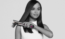 a black and white image of a woman using a dyson corrale to straighten her hair