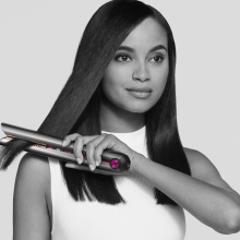 a black and white image of a woman using a dyson corrale to straighten her hair