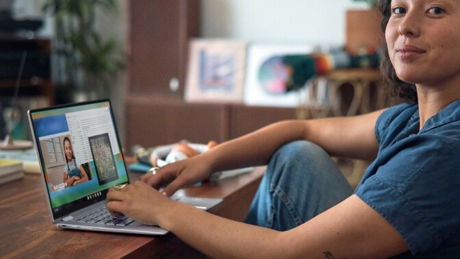 a person sits at a desk with a laptop in front of her while slightly smiling toward the camera