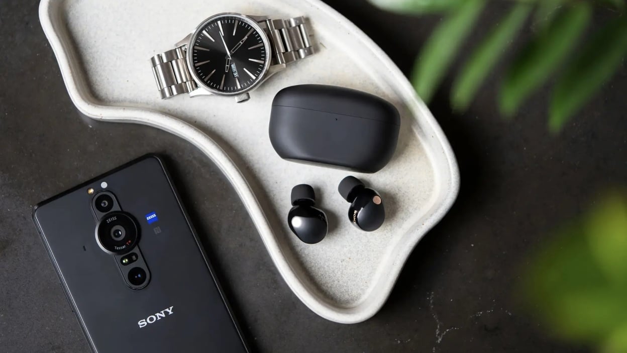 black sony wf-1000xm5 earbuds on tray next to watch and sony phone