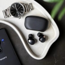 black sony wf-1000xm5 earbuds on tray next to watch and sony phone