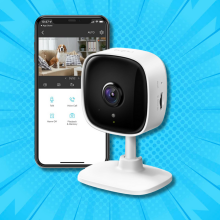 A TP-Link Tapo indoor security camera next to a smartphone displaying the camera's live feed of a dog in a room.