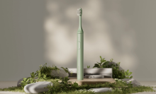 Green Suri electric toothbrush and charger displayed on rocks and moss