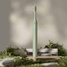 Green Suri electric toothbrush and charger displayed on rocks and moss