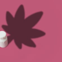 Illustration of a medicine bottle that casts a shadow of a marijuana leaf on a pink background with copy space