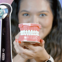 Black text on left side reads "Oral-B iO" against a light blue background. Girl with dark hair holds up a set of fake teeth to the camera.