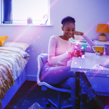 A young women in her dorm room surrounded by tech. 