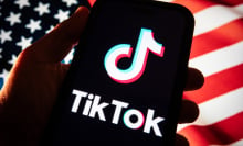 A hand holds out a phone with the TikTok logo in front of an American flag. 