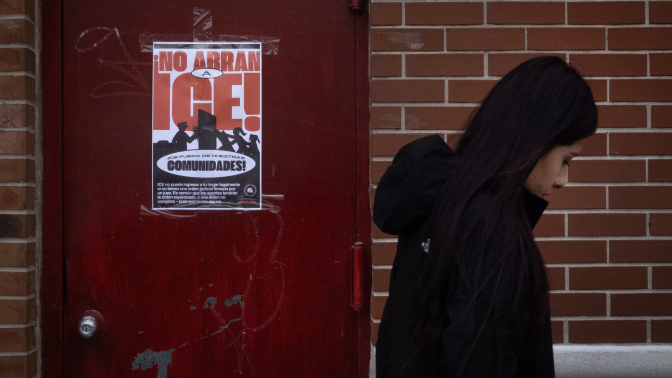 A woman walks in front of a poster that reads, "No abran a ICE!"