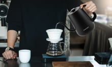 The Chefman gooseneck kettle held up by someone over a filter coffee maker in a kitchen.