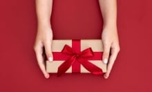 An overheard image of a gift box with red ribbon on red background.