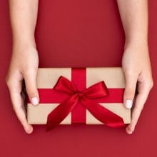 An overheard image of a gift box with red ribbon on red background.