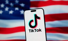 The TikTok app and logo are seen on a mobile device, the backdrop is the American flag. 