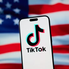 The TikTok app and logo are seen on a mobile device, the backdrop is the American flag. 