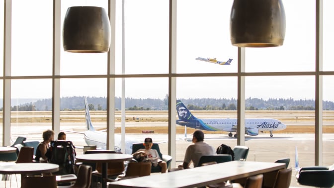 an airport lounge area with floor to ceiling windows that overlooks an Alaska airlines plane on the tarmac