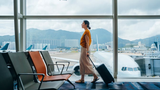 a person walks through an airport with empty chairs nearby while rolling a suitcase behind her. 