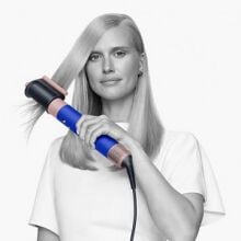 a person with long blonde hair uses the dyson airwrap hair dryer 