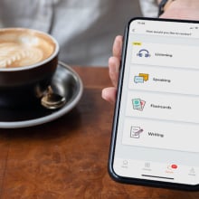 person holding up phone with babbel app next to coffee mug