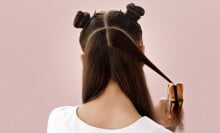 a person with long brown hair uses the dyson airstrait while standing in front of a pink background