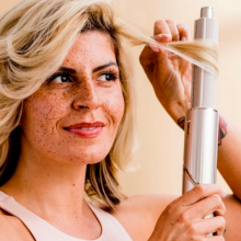 a close-up of a woman using a shark flexstyle to curl her hair