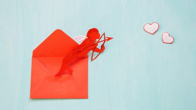 Cupid, made from paper, emerges from a red envelope over blue background.