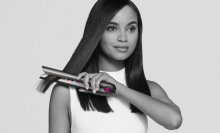 a black and white image of a woman in a white shirt straightening her hair with a dyson corrale