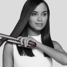 a black and white image of a woman in a white shirt straightening her hair with a dyson corrale