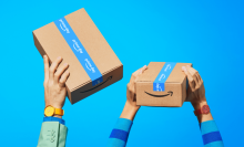 hands holding up Amazon Prime packages against blue background