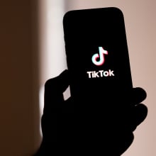 A backlit hand holds up a phone displaying the TikTok logo.