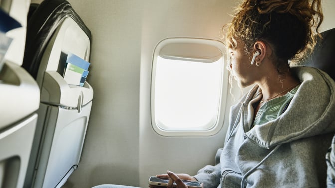 a young person looks out the window while sitting in the window seat on a plane