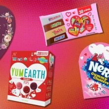 several packages of valentine's day candy including lindt truffles, yumearth lolipops and nerd clusters on a pink and orange background