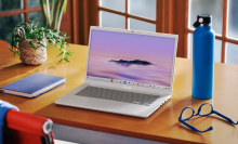 the asus chromebook plus cx34 on a wooden desk in front of a window next to a notebook, a water bottle, and a pair of glasses