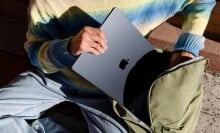 a person puts a black apple laptop into a green backpack