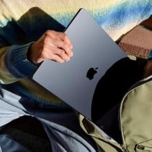 a person puts a black apple laptop into a green backpack